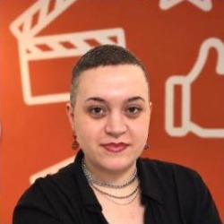Luana Rolim, pessoa branca de cabelos raspados nas laterais, usando colares e camisa preta, em fundo laranja com ícones.