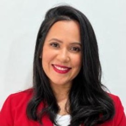 Luciana Alves, mulher de cabelos longos pretos, sorrindo, vestindo blazer vermelho, em fundo branco.