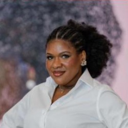 Márcia Silveira, mulher negra de cabelos cacheados presos, sorrindo, vestindo camisa branca.