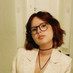 Marina Melo Abreu, mulher branca de cabelos curtos ruivos e óculos, vestindo blazer claro.