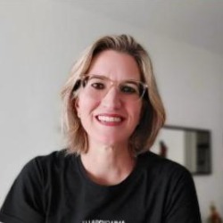 Suzeli Damaceno, mulher branca de cabelos loiros na altura dos ombros e óculos, sorrindo, vestindo camiseta preta.