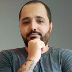 Vitor David, homem de cabelos curtos e barba, com a mão no queixo, vestindo camiseta cinza.
